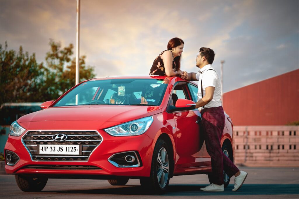 A young couple shares a moment by a red car, capturing love and modern lifestyle in Delhi's vibrant outdoor setting.