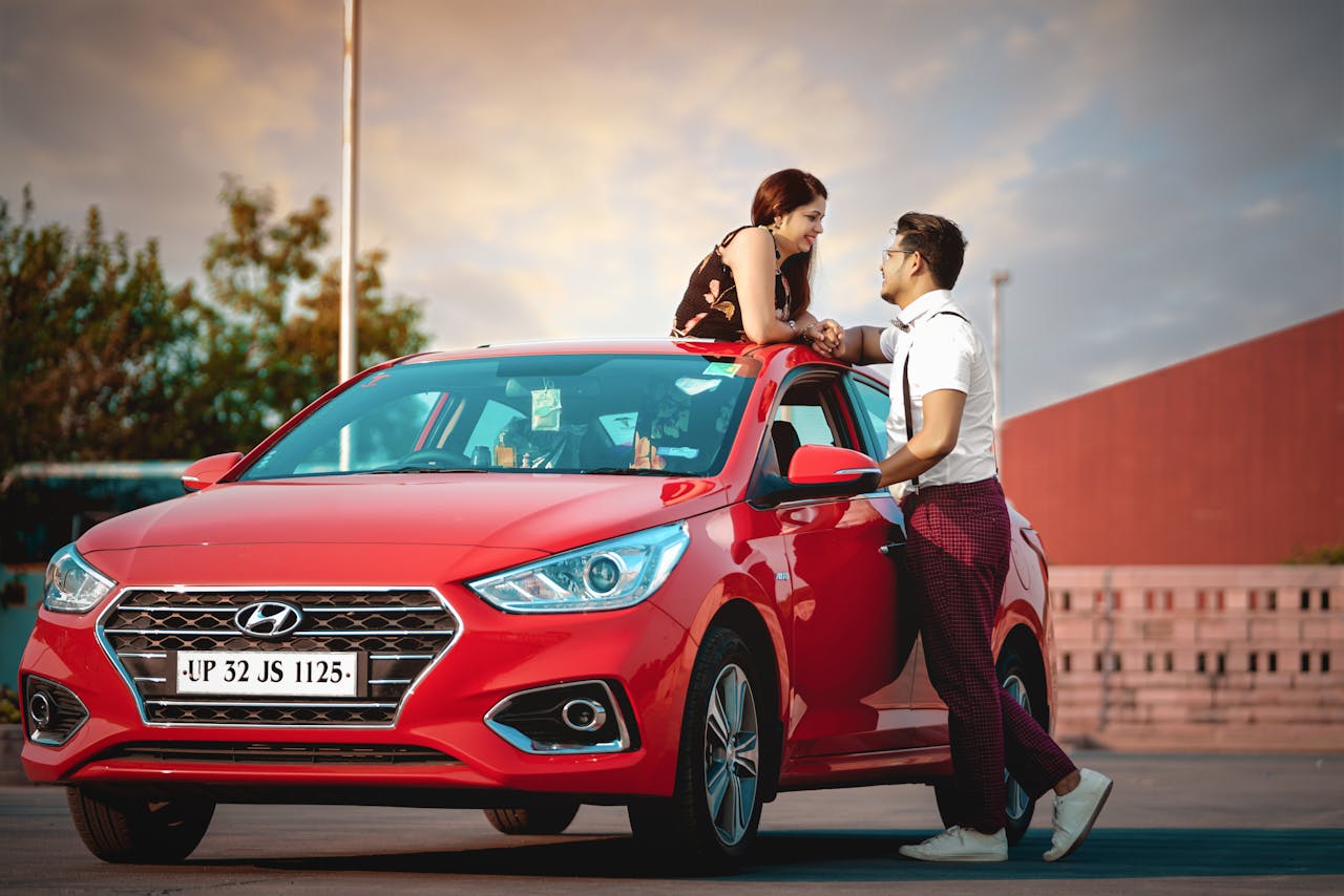 A young couple shares a moment by a red car, capturing love and modern lifestyle in Delhi's vibrant outdoor setting.